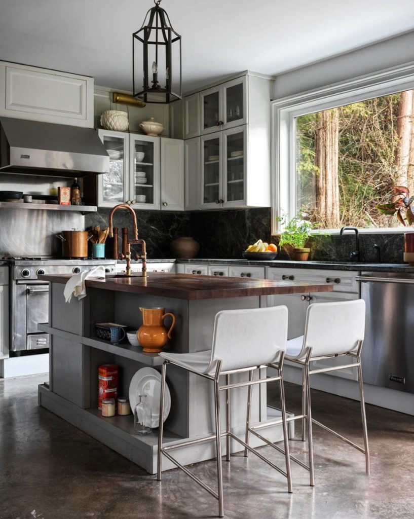 Kitchen with white cabinets and copper faucet with wooden island in the middle and stainless steel appliances, and white stools